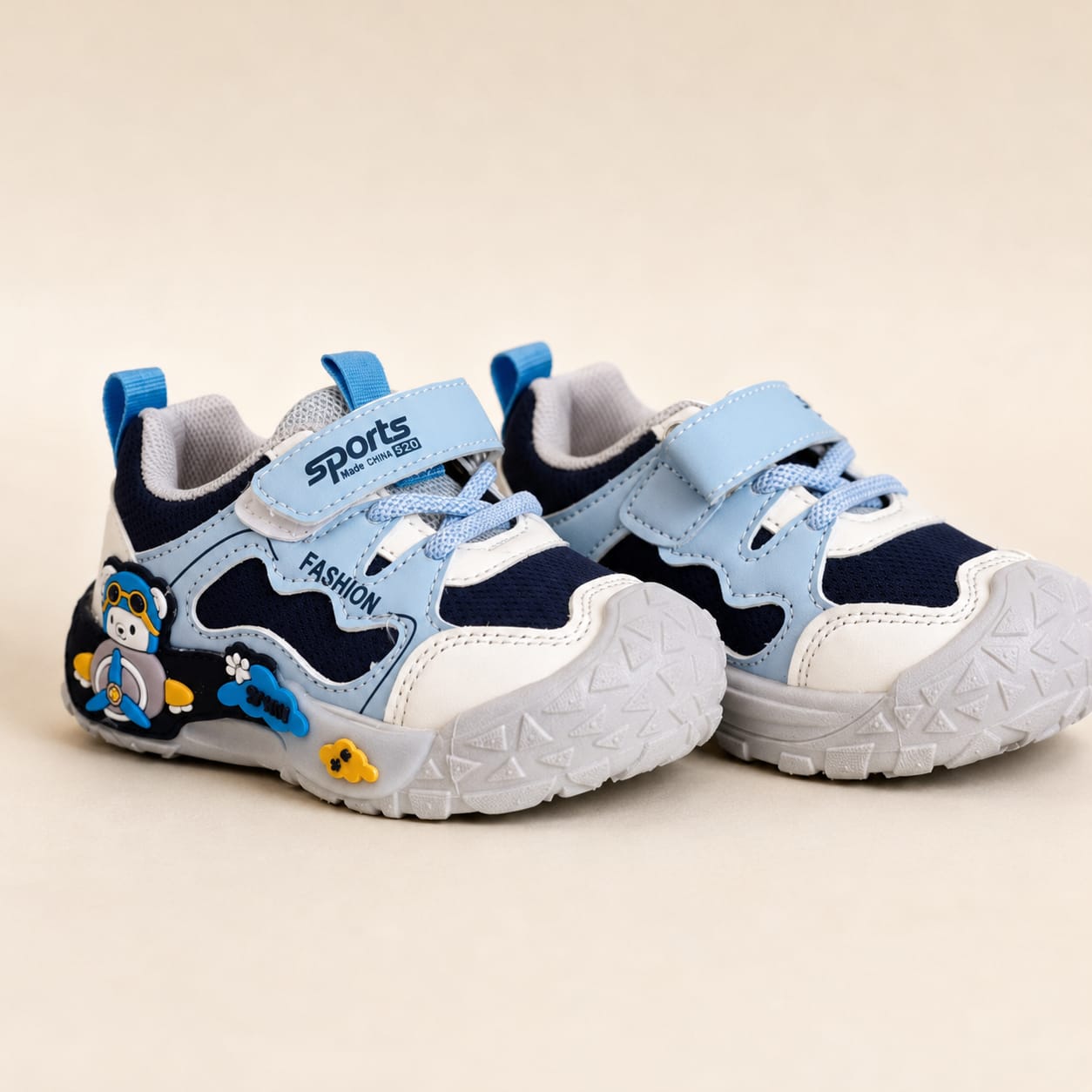 A pair of toddler sneakers in light blue, navy, and white, featuring hook-and-loop straps, cartoon penguin graphics on the side, and a textured white outsole, set against a plain beige background.